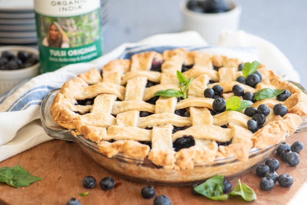 Holy Basil Blueberry Pie on a cutting board with fresh basil and blueberries. 
