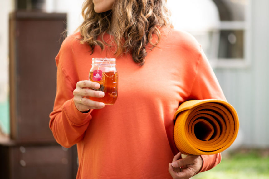 Women in orange sweater holding yoga mat drinking tulsi, one of the top adaptogens for energy