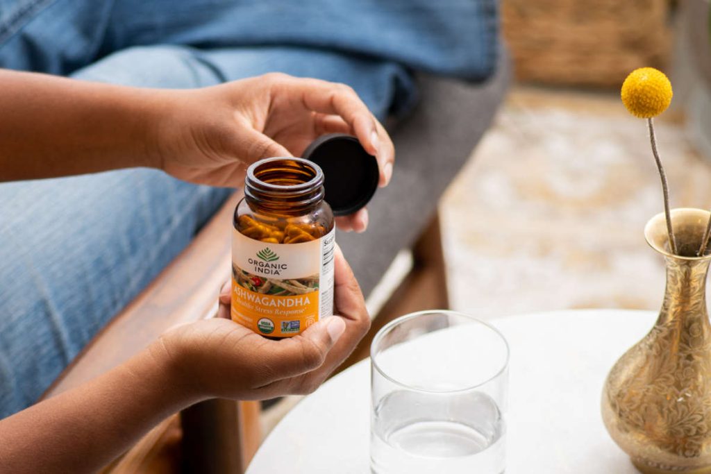 Woman opening a glass supplement jar of Ashwagandha capsules, an adaptogen vs nootropic.