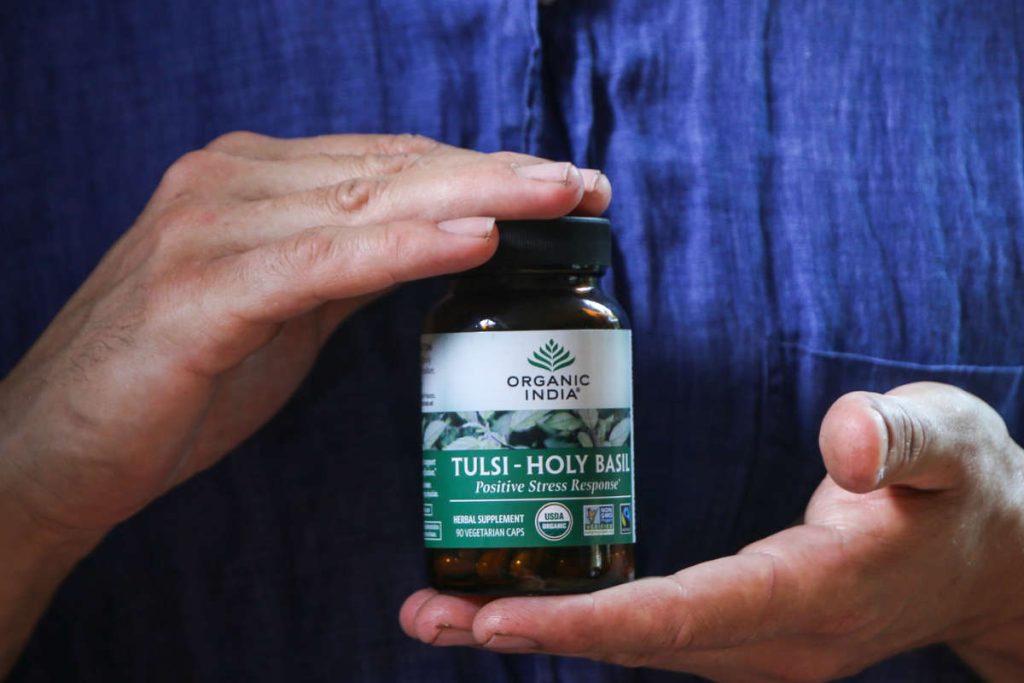 Man in blue shirt holding a glass capsule jar of Tulsi - Holy Basil  adaptogen