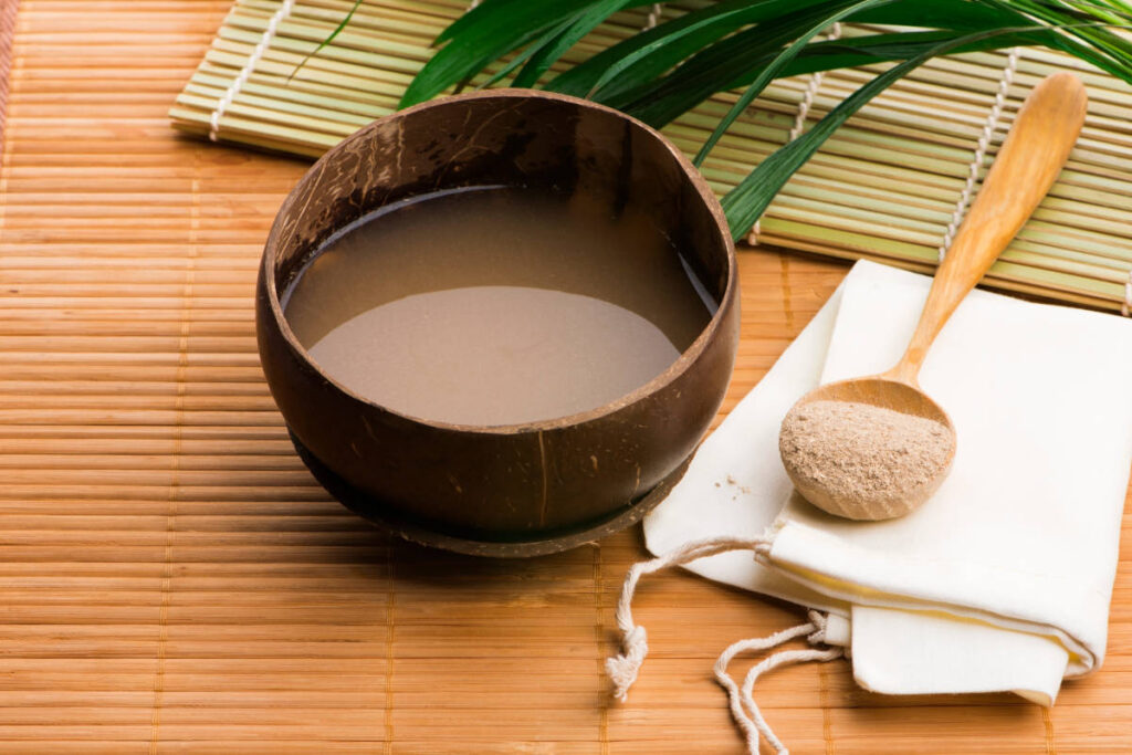 A cup of kava on a straw table in a coconut shell with a scoopful of kava powder.