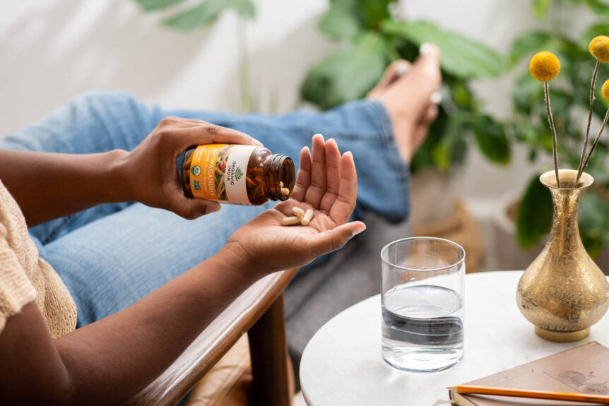 Woman in chair taking ashwagandha for sleep or energy capsules on a sunny afternoon in the living room.