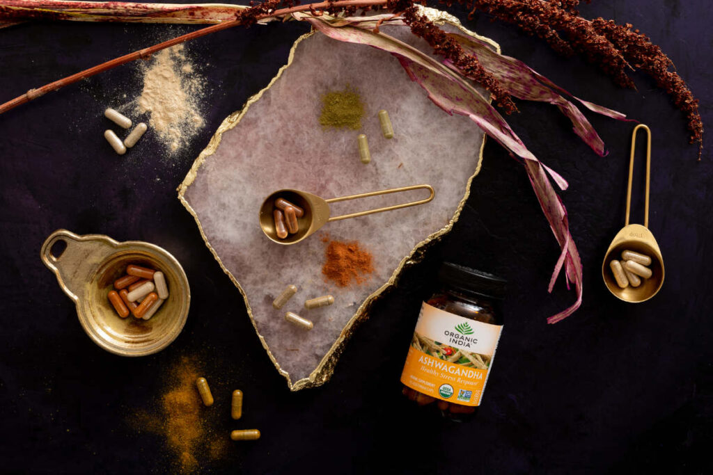 ashwagandha/indian ginseng supplement capsules, powder and glass jay on black table with stone and dried plants.