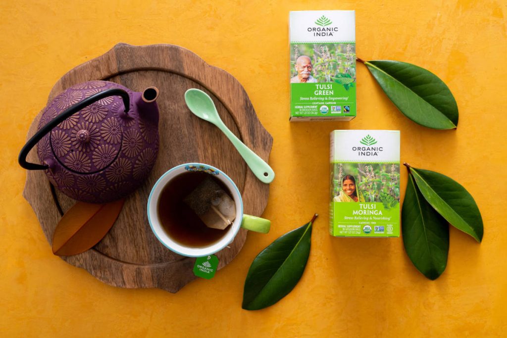 Tulsi Green and Tulsi Moringa ayurveda teas for detox on a yellow table with cast iron tea kettle.