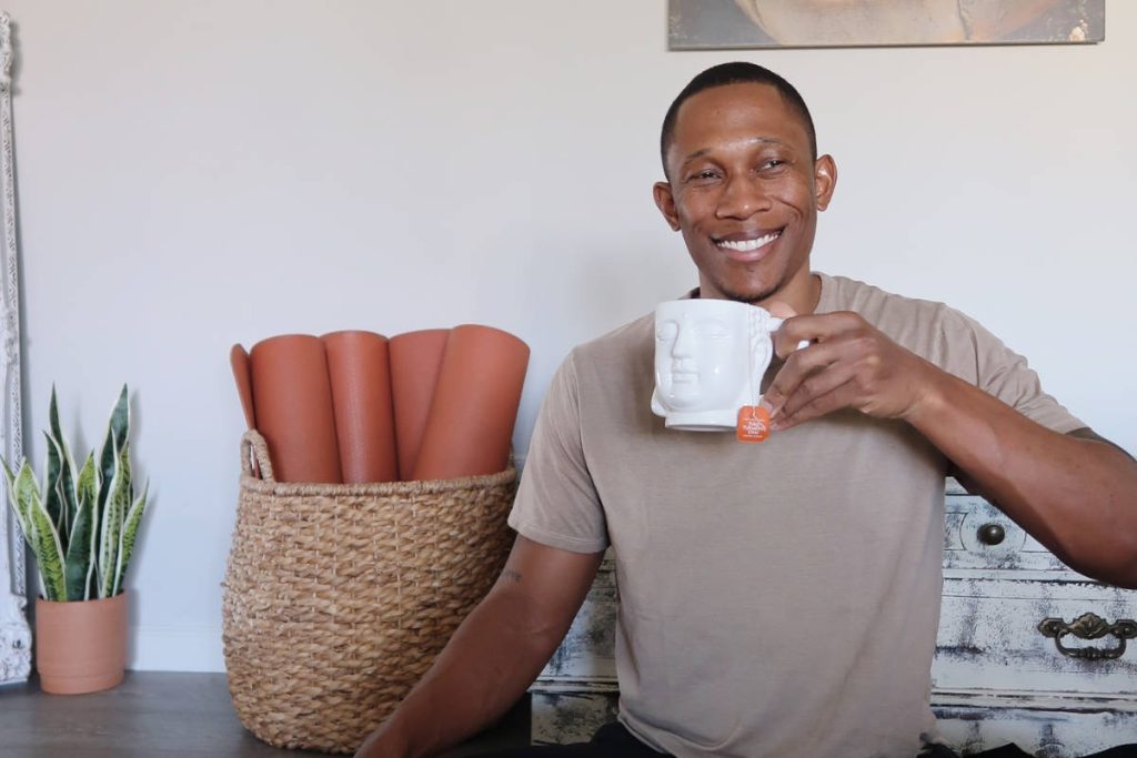 Man drinking herbal cleanse tea from a buddha shaped cup in a yoga studio.