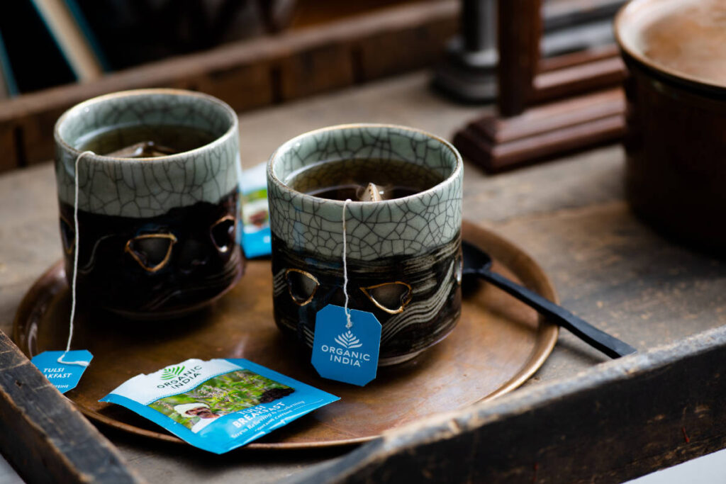 Two ceramic mugs of Tulsi Breakfast tea on copper plate atop wood serving tray, with bacopa for brain health.