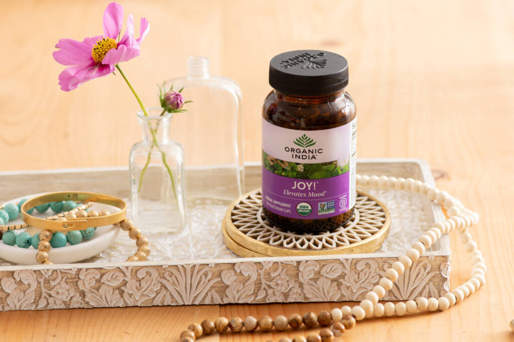 Bacopa with Gotu Kola, Shankhpushpi and Ashwagandha in this organic joy supplement on an ornate platter on wood table with mala bead necklance.