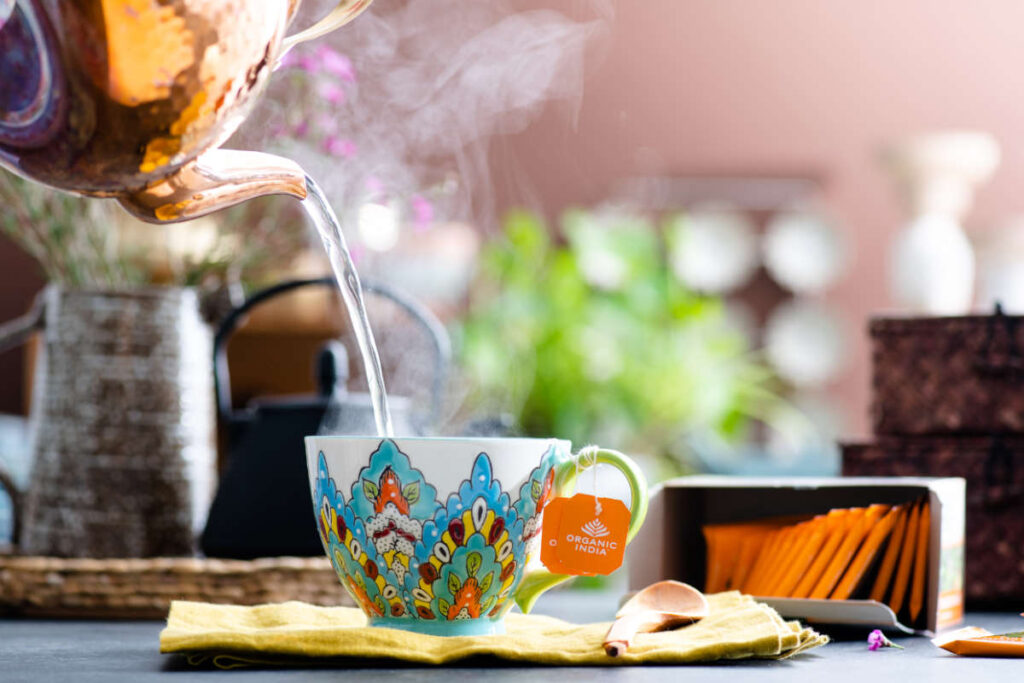 Benefits of Tulsi tea in a ceramic floral teacup and copper pot.