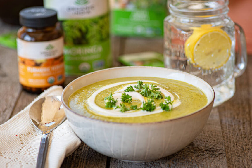 Broccoli detox soup in a white ceramic bowl with fresh herb and yogurt garnish.