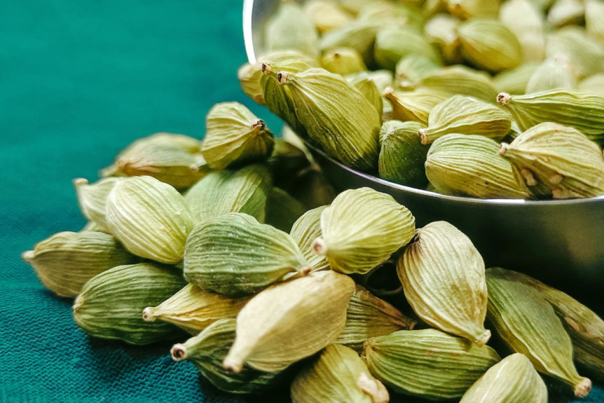 A bowl overflowing with green cardamom on a deep green tablecloth