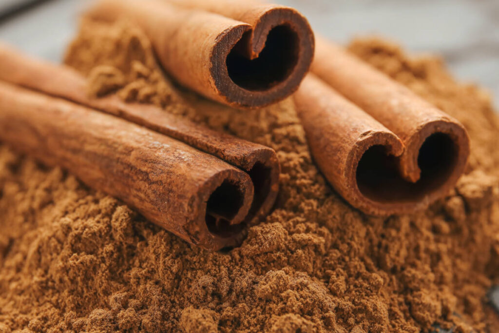 Whole cassia cinnamon sticks on a bed of cassia cinnamon powder.