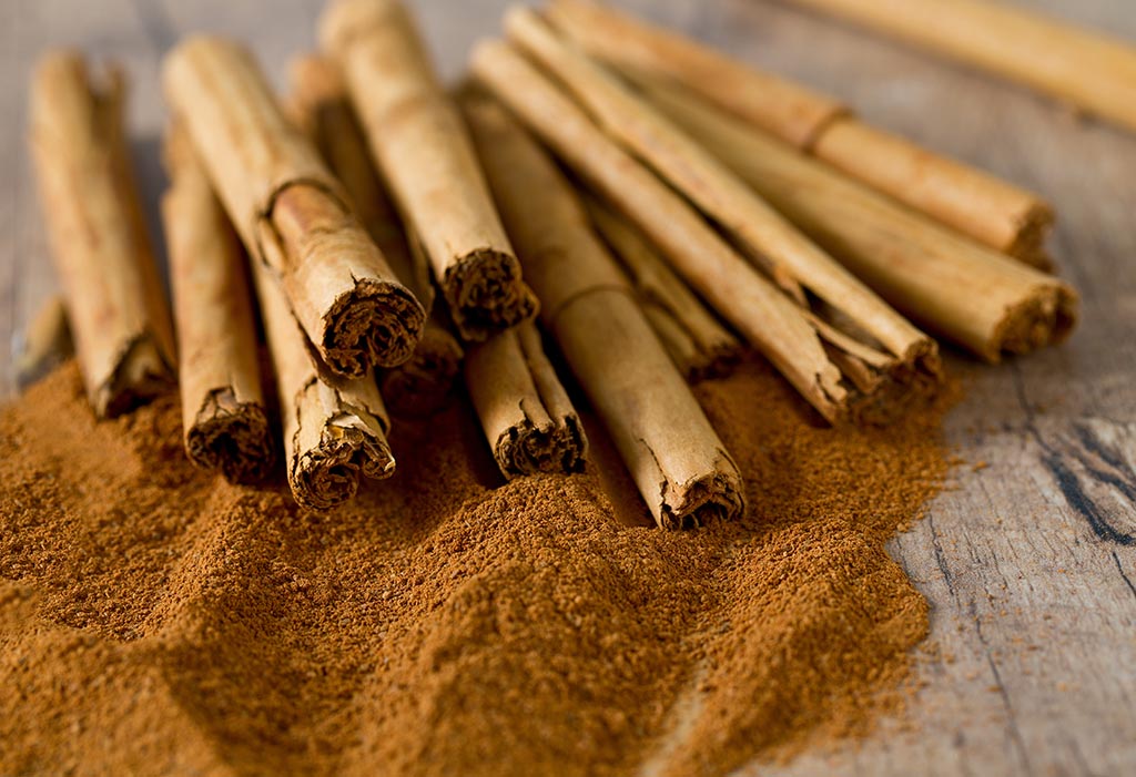 Ceylon cinnamon sticks piled on top of powdered cinnamon on a wood table. 