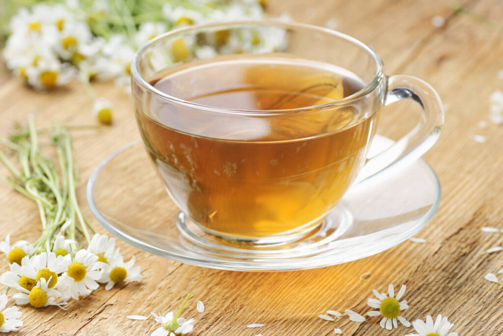 a little cup of chamomile surrounded by flowers on a wooden table for skin benefits.