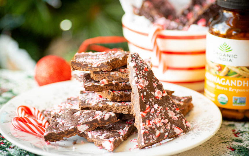 Festive chocolate peppermint bark with adaptogen Ashwagandha on a white plate with decor surrounding.