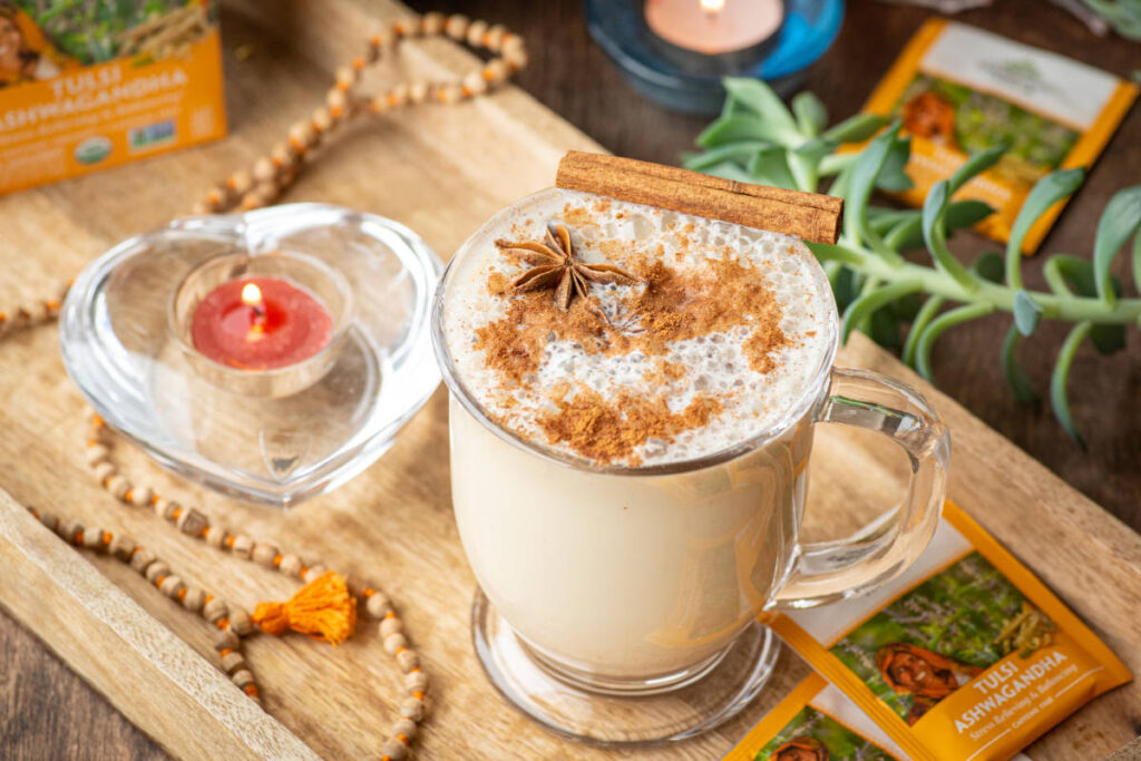 Cinnamon ashwagandha latte in a clear mug with fresh cinnamon and star anise on a wooden serving tray with candle.