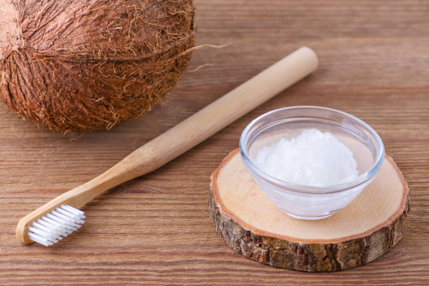 Coconut oil pulling in clear glass jar with wooden tooth brush and fresh whole coconut.