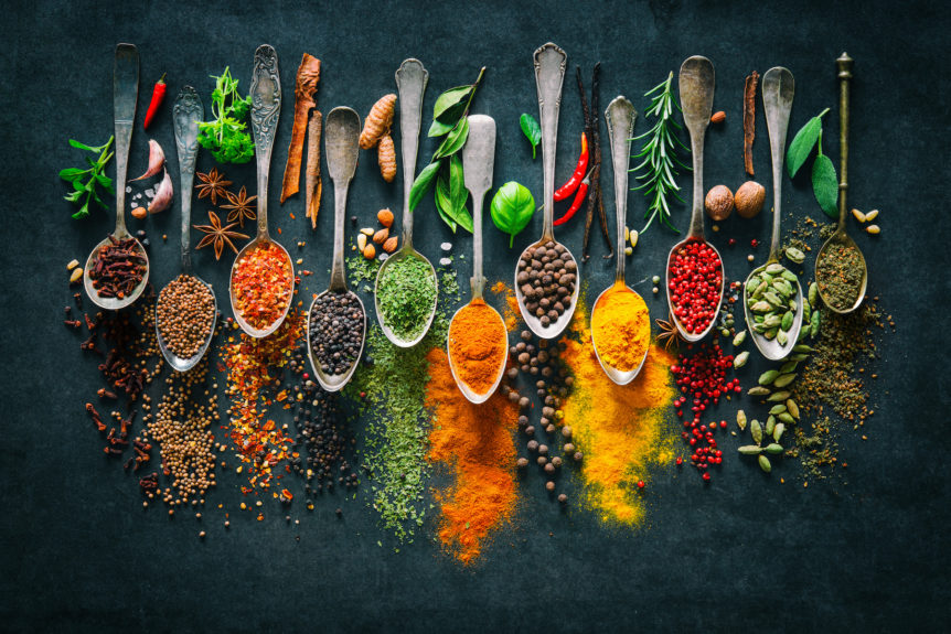 Ayurvedic herbs and spices in whole and powdered form on spoons.
