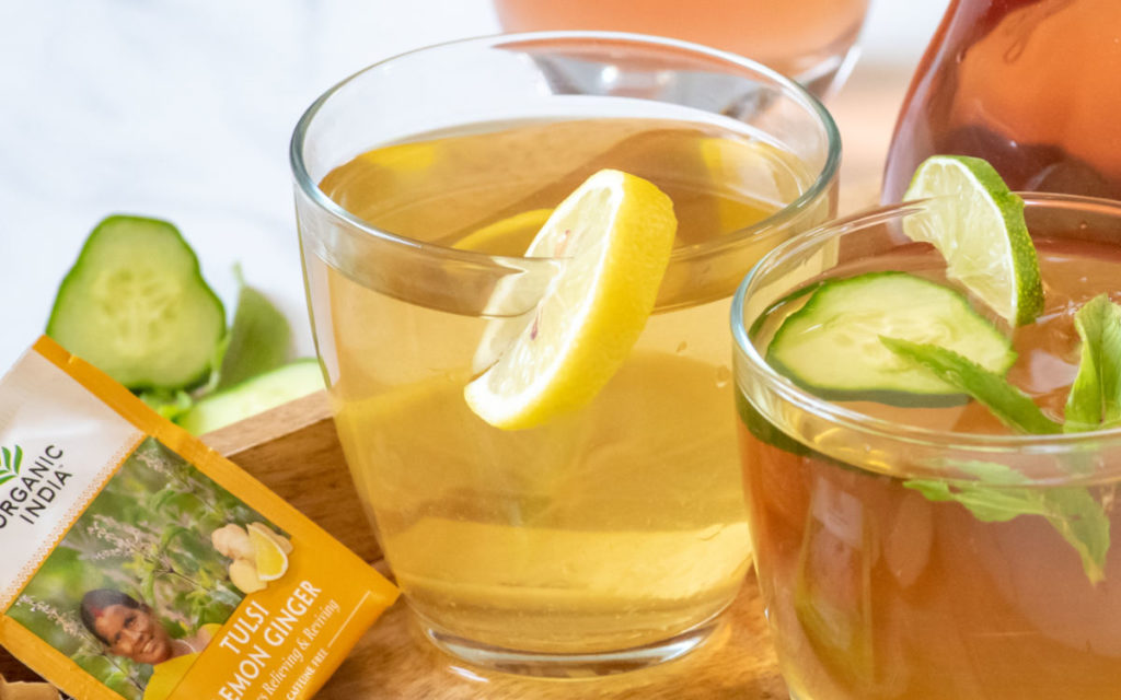 Lemon ginger detox iced tea in a glass with lemon as garnish and Organic India tea bag to the left. 
