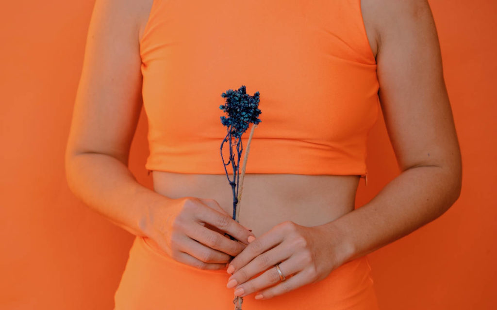 Woman holding herb in front of her belly wearing orange outfit. 