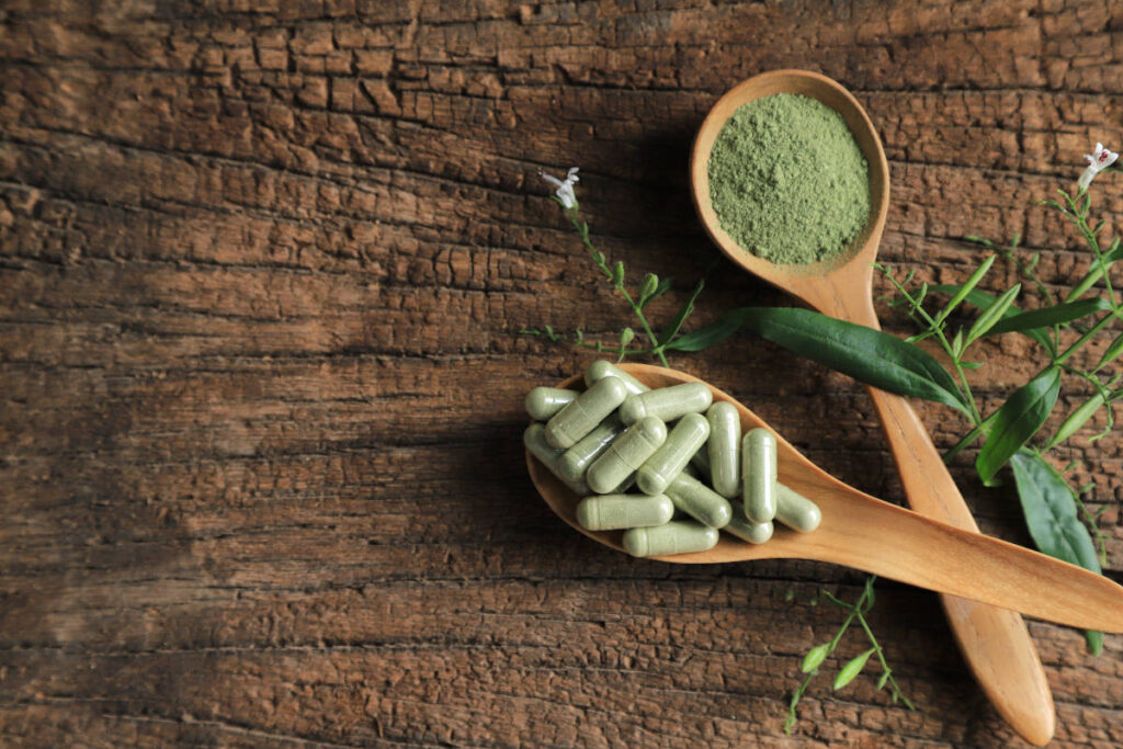 Andrographis powder, leaves and capsules in wooden spoons on a wooden table. 