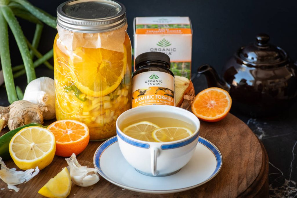 Fire cider in a large mason jar with turmeric, orange, lemon, garlic, ginger and a cup of tulsi turmeric ginger tea.