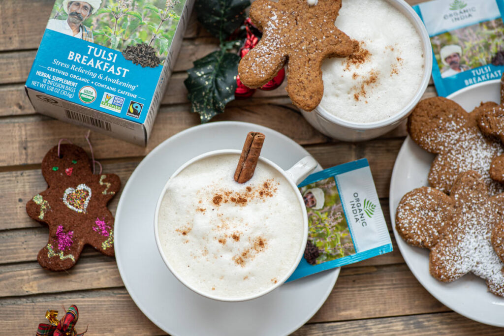 Gingerbread tea latte on wooden table with gingerbread cookies and organic india tulsi breakfast tea.