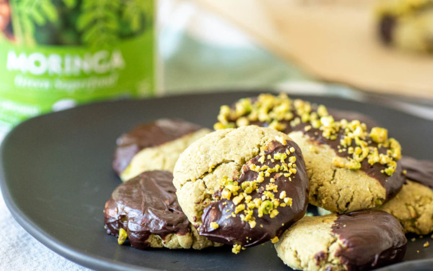 Pistachio cookies with moringa and chocolate on a black plate.