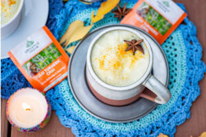 golden chai latte with star anise and turmeric garnish on blue knitted kitchen towel by candle.