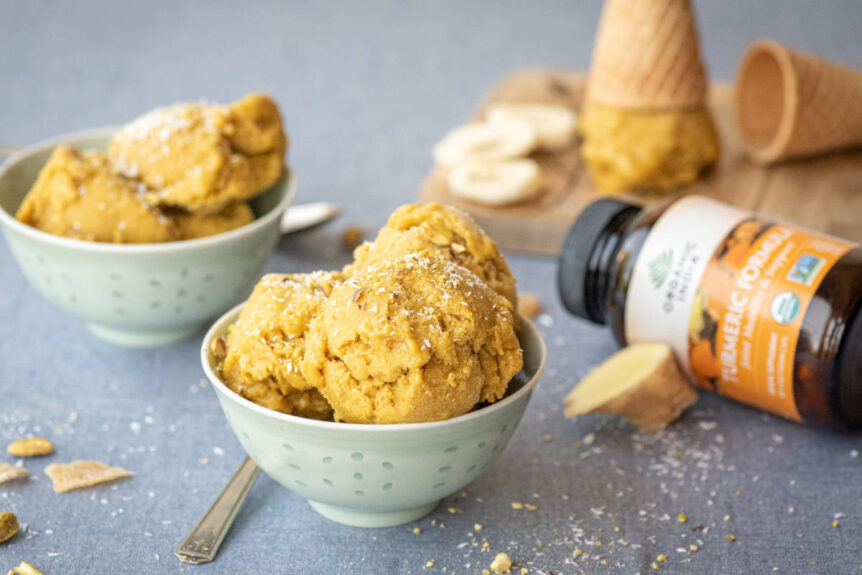Golden turmeric ice cream in a small sage green dessert bowl with turmeric capsules