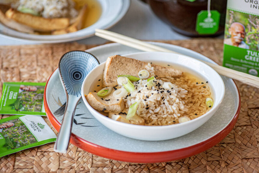 Green tea soup with tofu and rice in a white bowl beside a large ceramic tea spoon.
