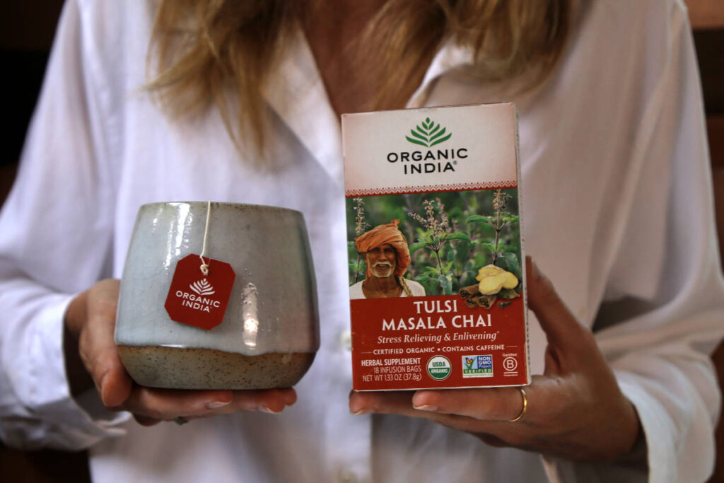 Woman holding tea box and mug of Tulsi Masala Chai, featuring black tea vs green tea.