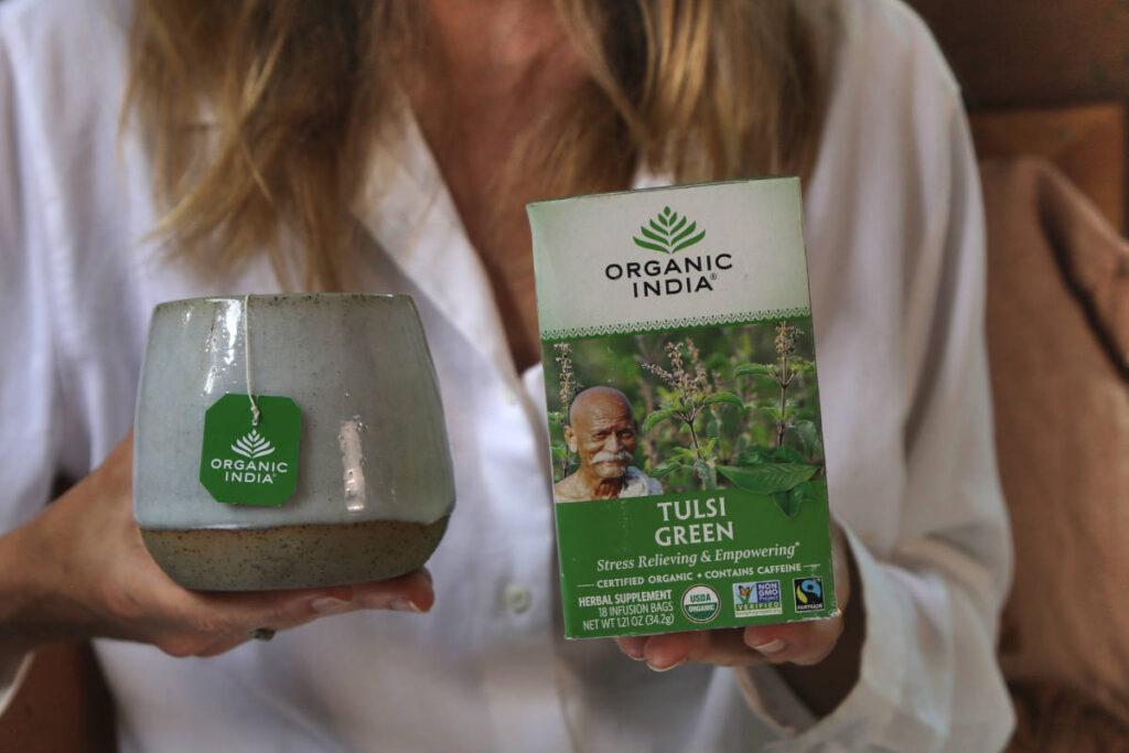 Woman holding tea box and mug of Tulsi Green, featuring green tea vs black tea.