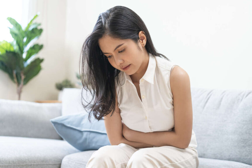 Woman with some gut health and digestive issues looking a bit distressed on couch near plant.