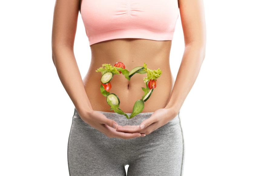 Woman with heart of veggies on her stomach to show the link between digestion and gut health.