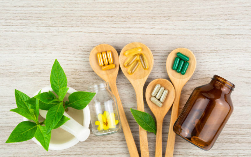 Multiple supplements for herbal pairings on a wood table with wooden spoons.