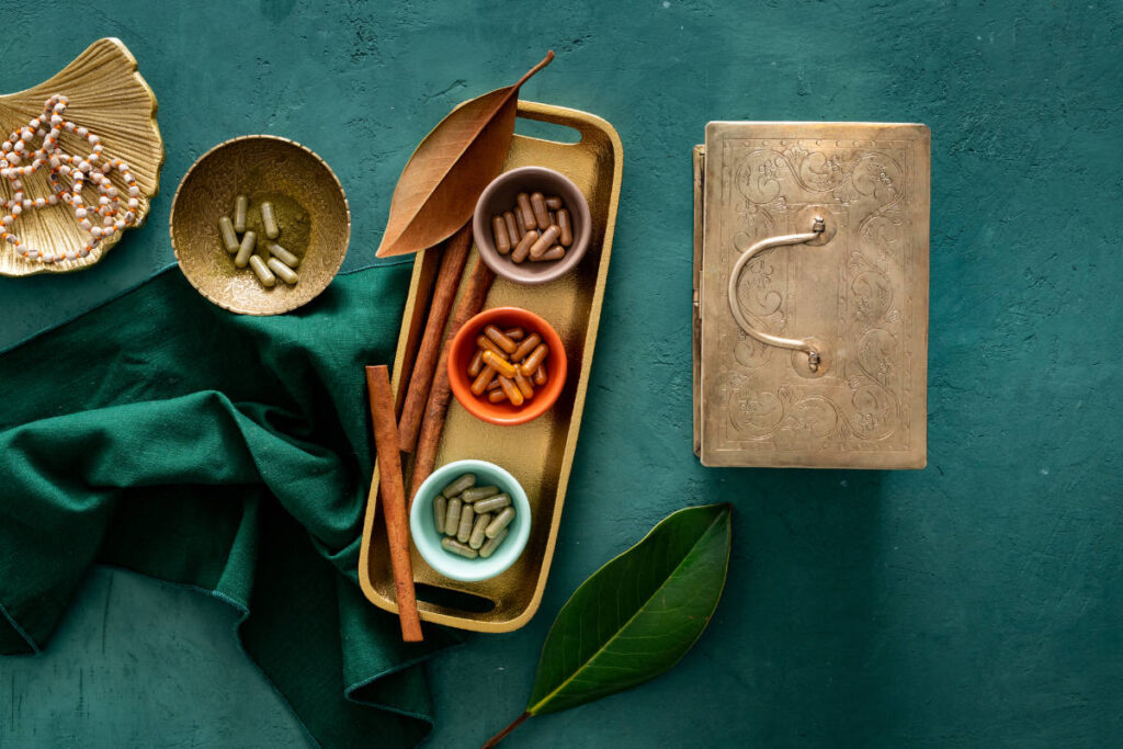 Herbal wellness capsules in little cups and copper box on green texture table 