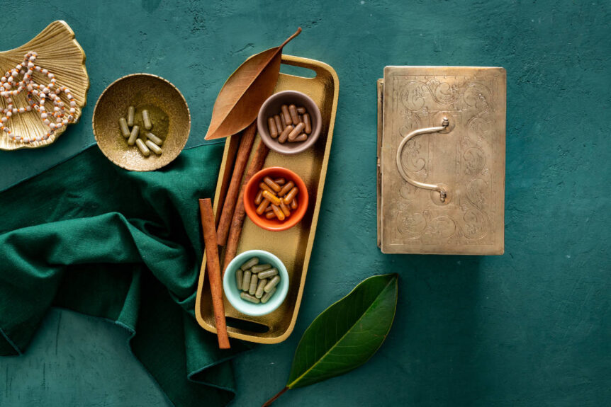 Capsules containing spices and herbs for detox in copper bowls on a green textured table.
