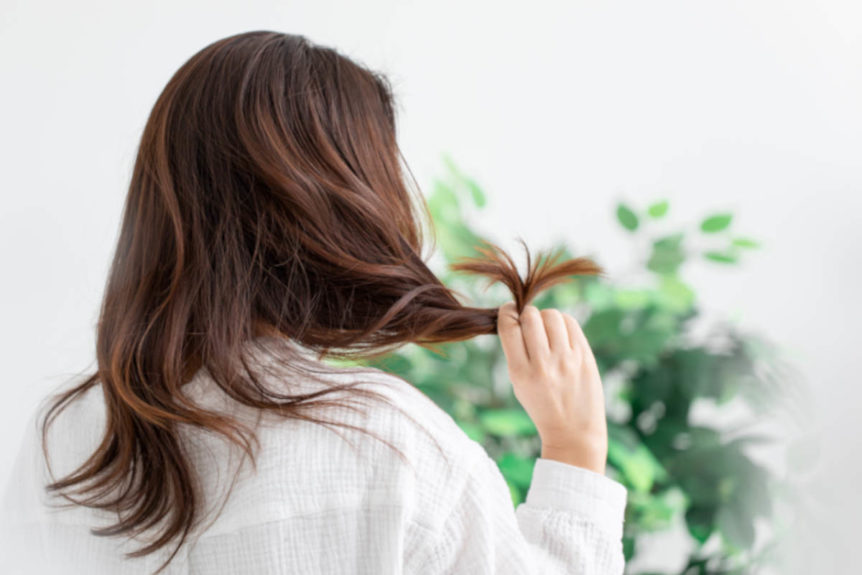 Woman with brown hair and white shirt and plants contemplating herbs for hair.