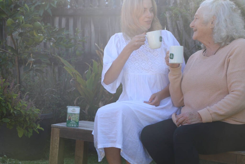 Grandmother and granddaughter drinking herbs for healthy aging tea on a bench in the garden.