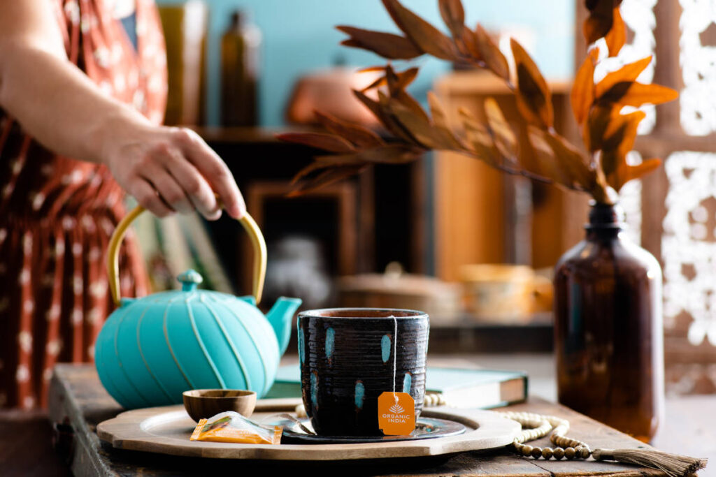 Woman in orange dress pouring teal tea kettle with herbs for fasting.