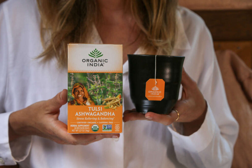 Woman in white shirt holding a black mug of Tulsi Ashwagandha infusion