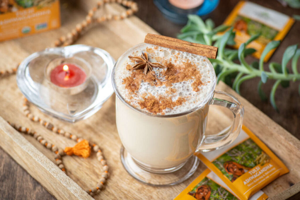 Cinnamon spice and a cinnamon stick adorning a cinnamon latte in a glass mug. 