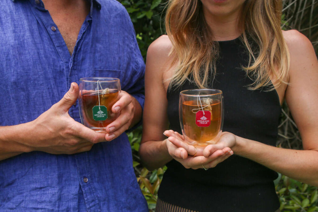 Man and woman standing beside each other each holding a clear mug of fresh brewed tulsi tea, an herb for love.