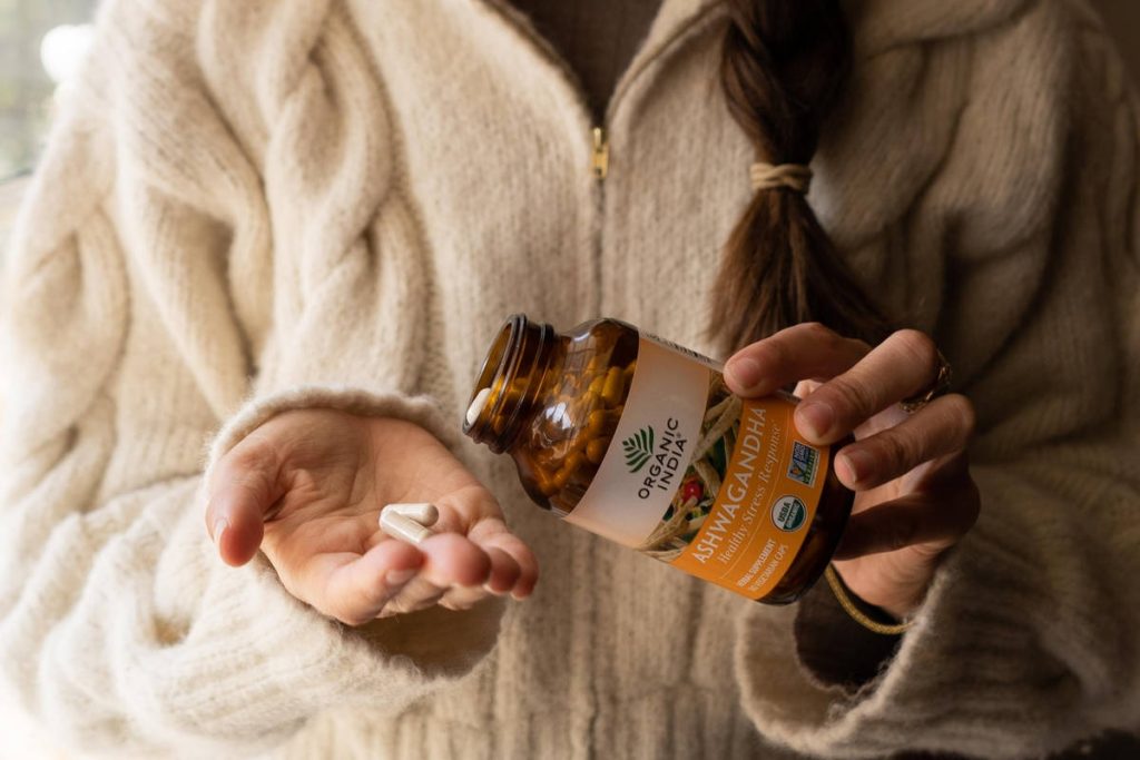 Woman in fluffy beige jacket taking ashwagandha capsules.