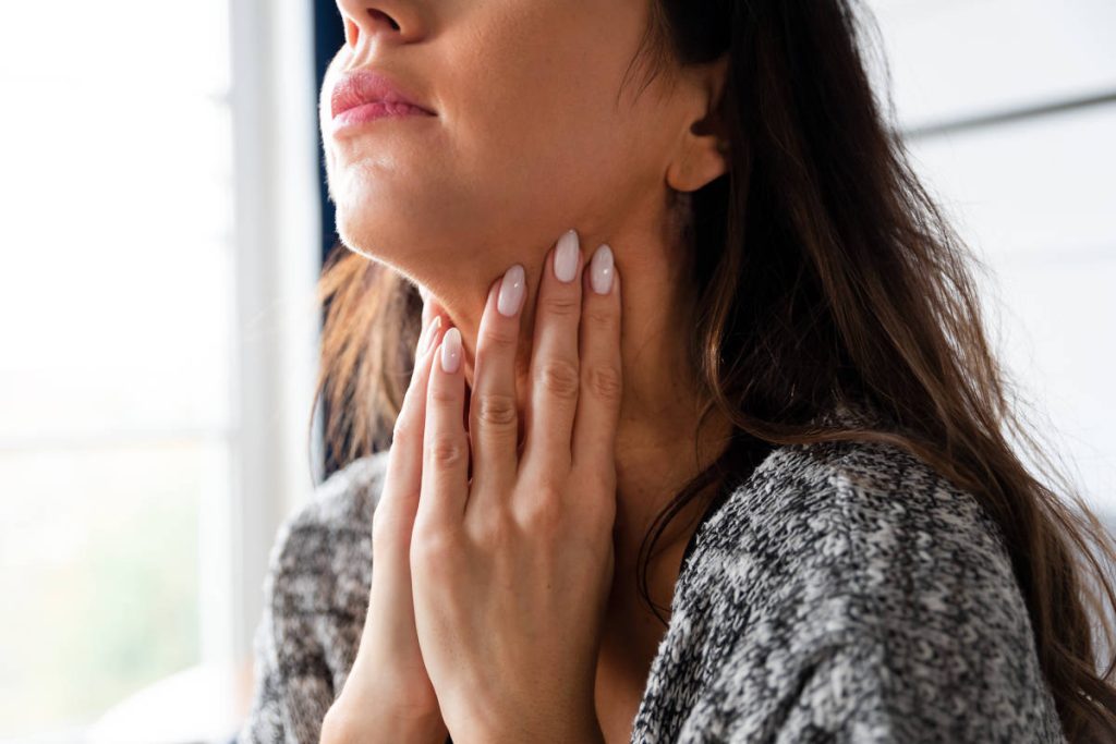 Woman with hands to thyroid after taking herbs for thyroid at home.