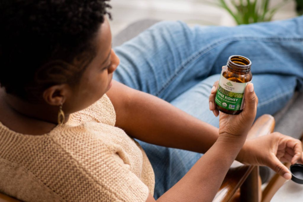 Woman in jeans sitting in living room taking liver kidney, which contains punarnava, an herb for thyroid health.