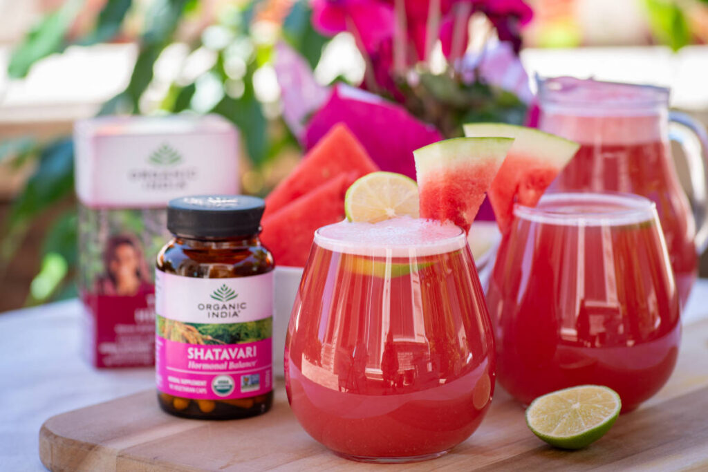 Hibiscus agua fresca with watermelon and lime garnish in clear glass on wood cutting board.