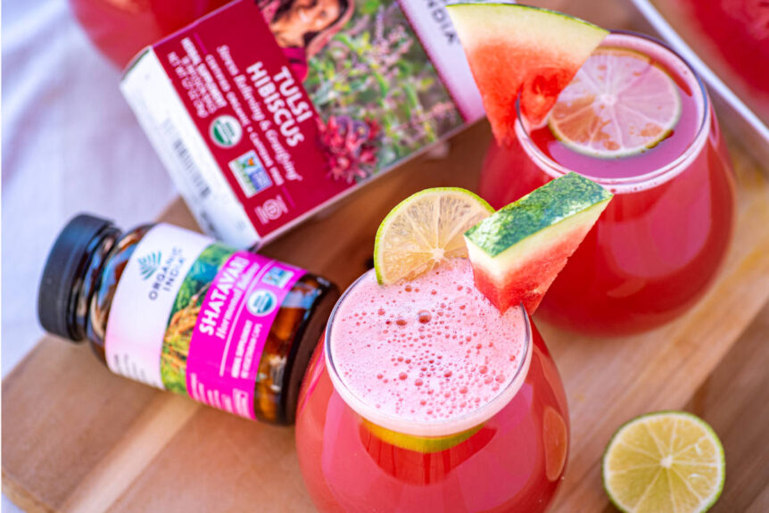 Hibiscus agua fresca with watermelon and lime garnish in clear glass on wood cutting board.