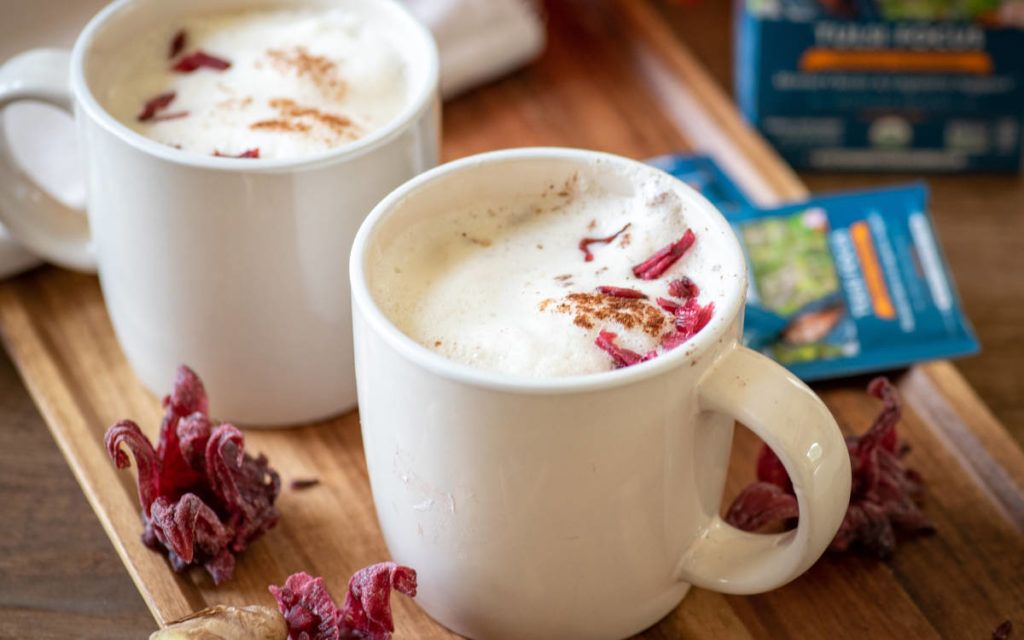Hibiscus cinnamon tulsi holiday latte with dried hibiscus garnish in white mug on wooden cutting board. 