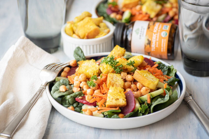 Homemade Turmeric croutons over a salad in white bowl.